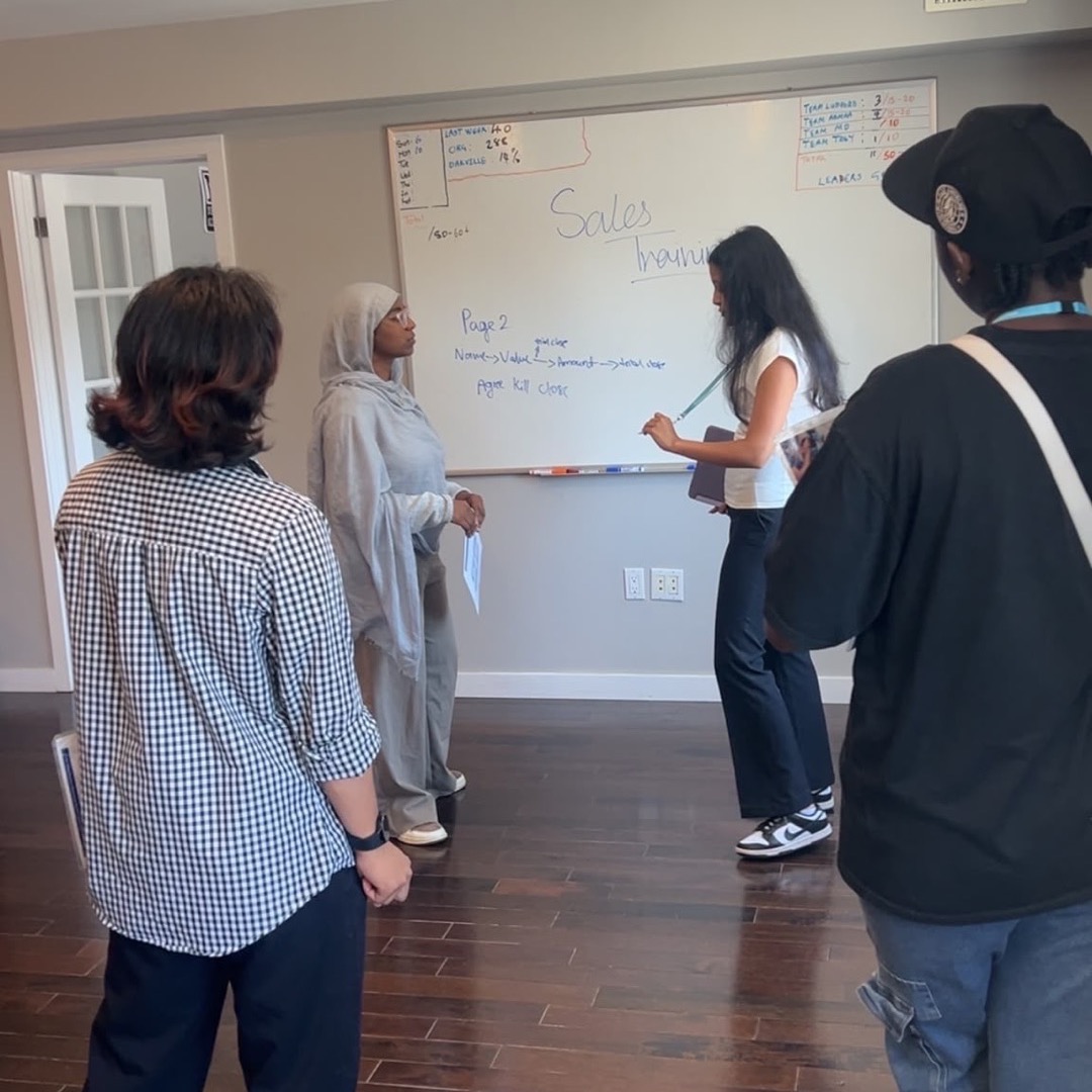 Sales training session — a leader walks the team through the pitch on the whiteboard.